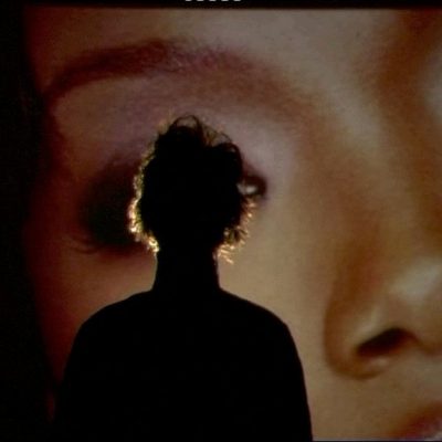 Image of Mark Leckey's: Parade, 2003. A man is silhouetted against a larger photograph of a woman's face.
