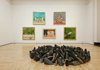 Image of a gallery within the National Museum in Cardiff. A collection of stones have been collected into a circle, in front of a collection of paintings.