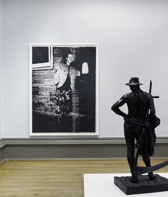 Image of Wolfgang's Tillmans' Installation at Walker Art Gallery in 2010. A statue of a topless man holding a scythe facing away from camera, and a large grainy photograph of another man.