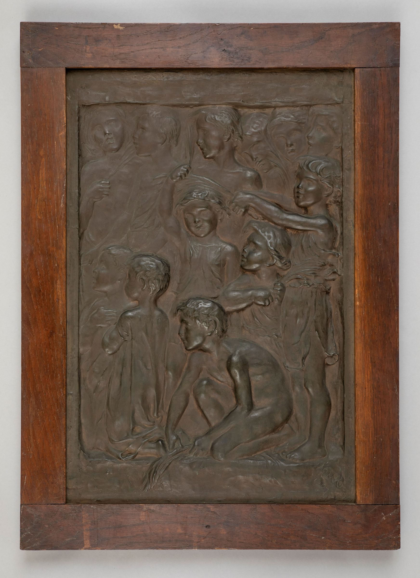 a relief sculpture in dark bronze of a group of children looking in the same direction to the left