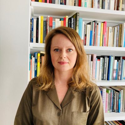 portrait of Jennifer, standing in front of a bookcase wearing an olive green shirt