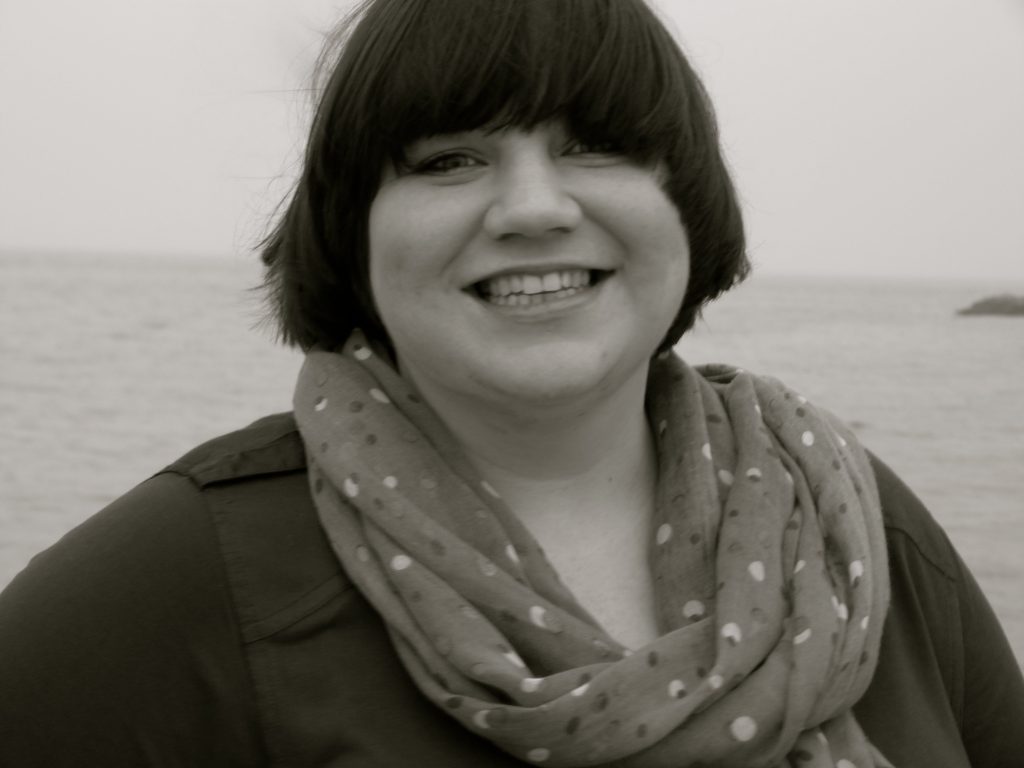 black and white portrait photograph of Helen Pritchard smiling at the camera, seascape behind