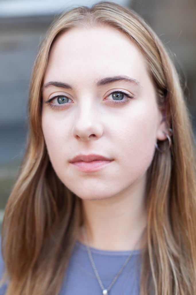 portrait photograph of Holly looking directly at the camera, in close up, a blurred architecttural background