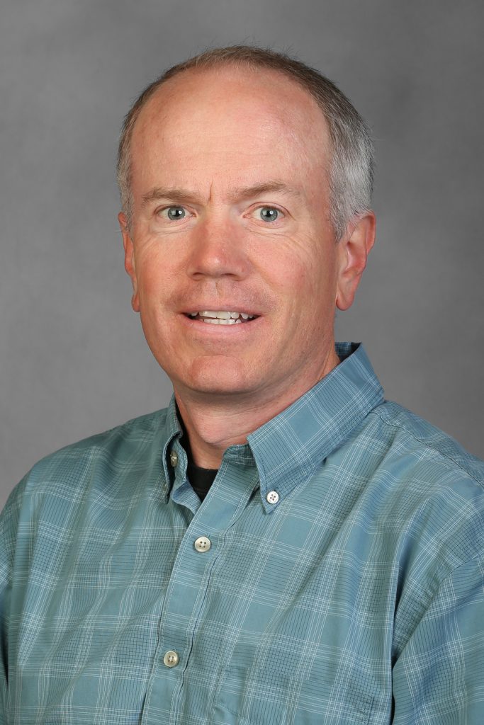 portrait photo of Andrew, head and shoulders, looking directly at camera mouth slightly open, plain grey background