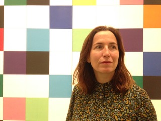 portrait photo of Charlotte in front of an abstract geometric painting, a grid of blues, purples, pinks purples and white squares