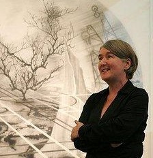photo of Gill standing, seen from side looking out of shot to the left, a large near-monochrome artwork featuring tree forms and other organic shapes, and lines, behind
