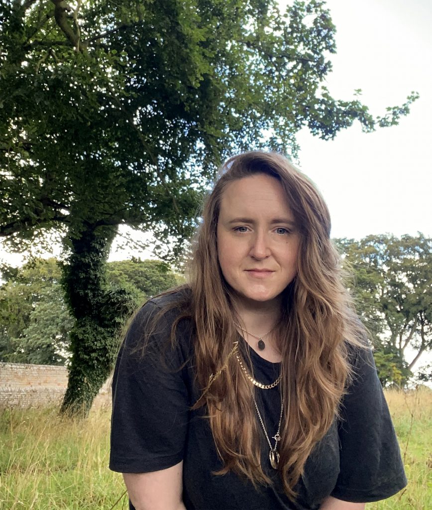 portrait photo of Katherine, half length, standing outside with grass and trees behind