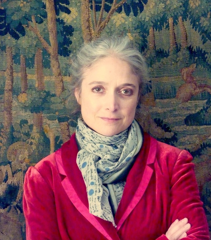 head and shoulders portrait of Susan, arms crossed looking directly at camera, a wall tapestry behind