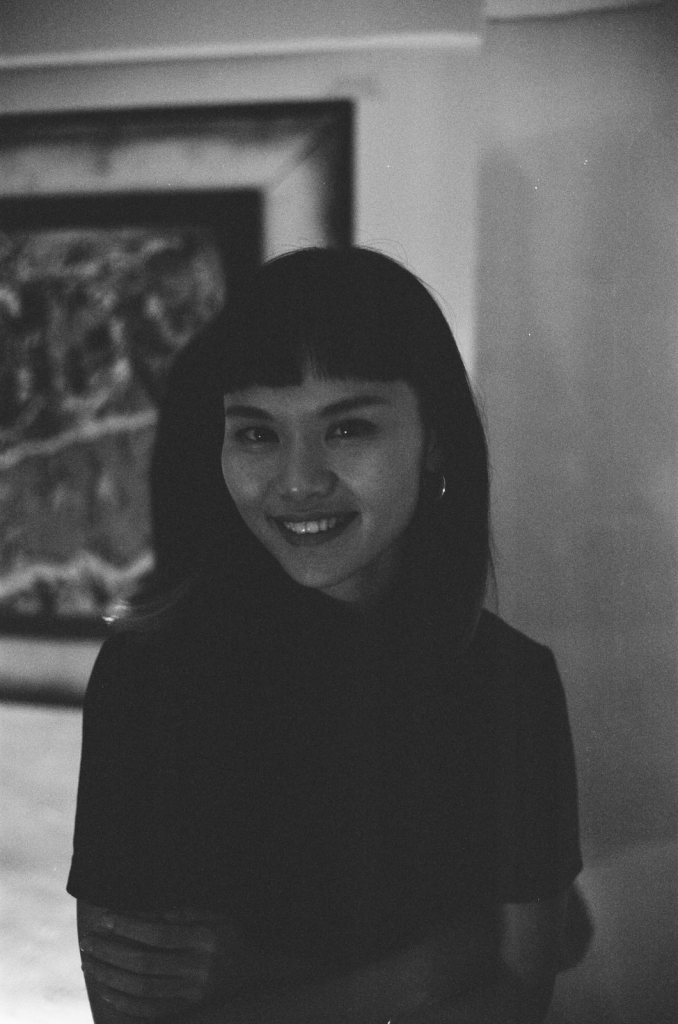 black and white portrait photo of Jessica, half length, smiling, with a framed work of art behind