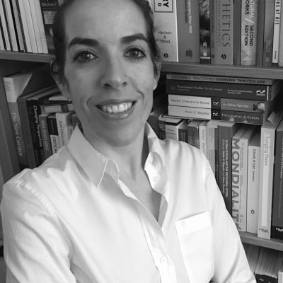 black and white portrait image of Raquel, arms crossed, smiling, in front of filled bookshelves