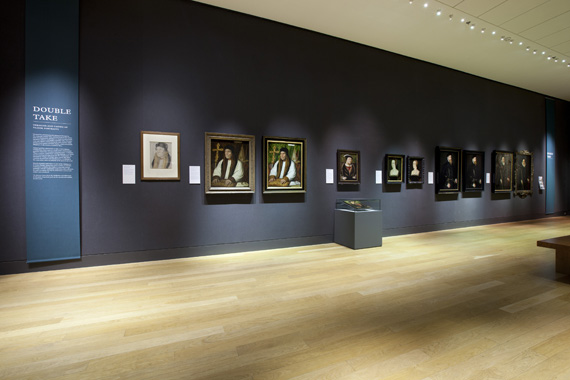 gallery view, Tudor portraits on dark blue walls, dramatically lit - some portrait images appearing more than once