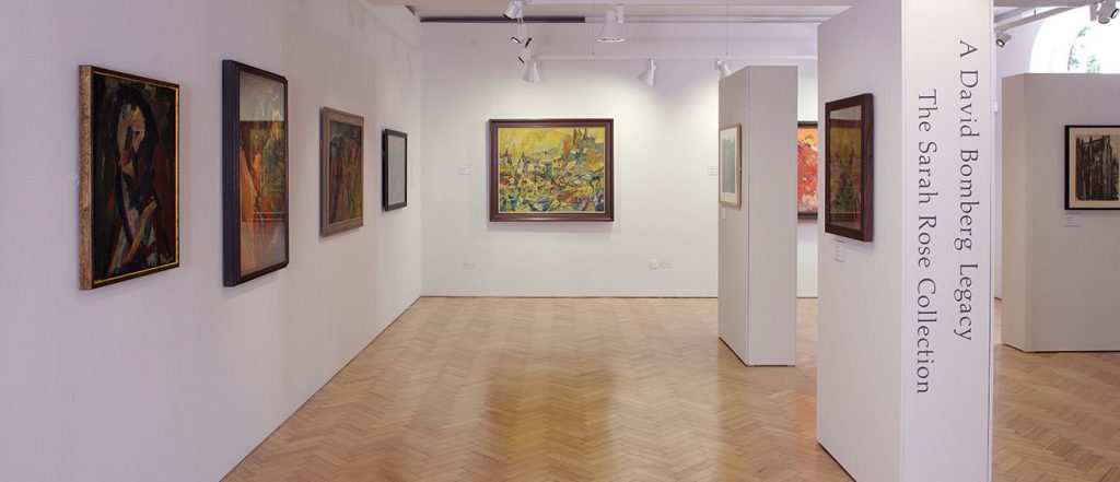 gallery interior, wooden floor, white walls, with strongly coloured, expressive figurative paintings on the walls