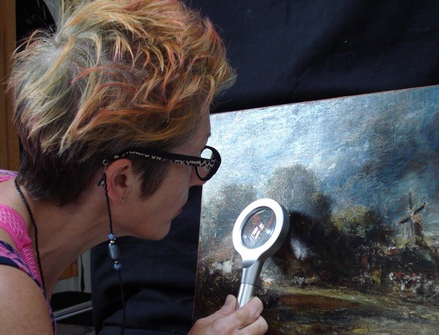 photo of Sarah, from behind closely examining a Constable painting with a specialist-looking device