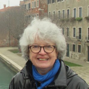 portrait photo of Sheila smiling and looking directly at camera, on a bridge in Venice, historic buildings along canal in background
