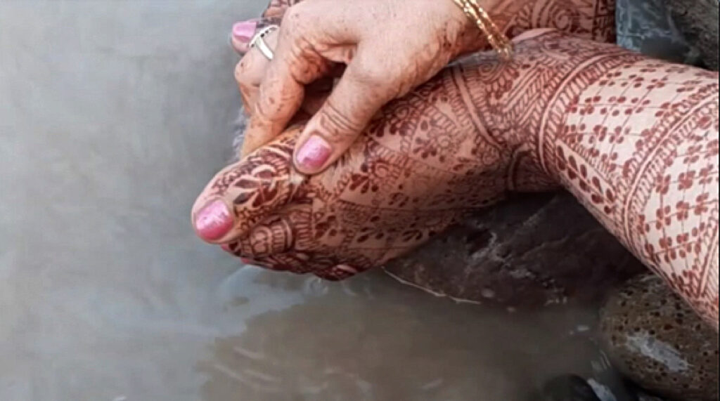 close up view of a foot and hand clasping it gently , both heavily decorated with henna, the nails painted pink