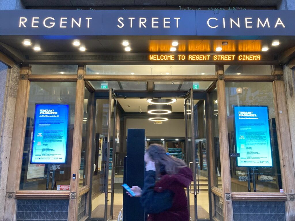 streetview of historic cinema frontage, 'Regent Street Cinema' sign above, digital screens advertising 'Itinerant Imaginaries' screenings in large windows to left and right - blurred figure walking before the doorway in the middle of this symmetrical view
