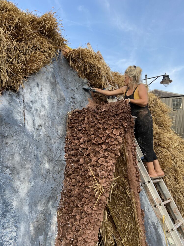 A person stands on a ladder leaning against a structure made of hay, plaster, and clay.