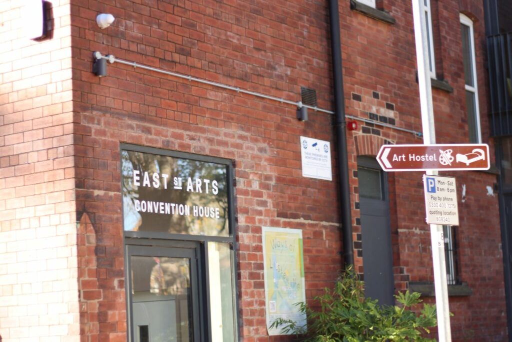 The words 'East Street Arts Convention House' above the entrance to a red brick building. A street sign labelled 'Art Hostel' points towards the building.