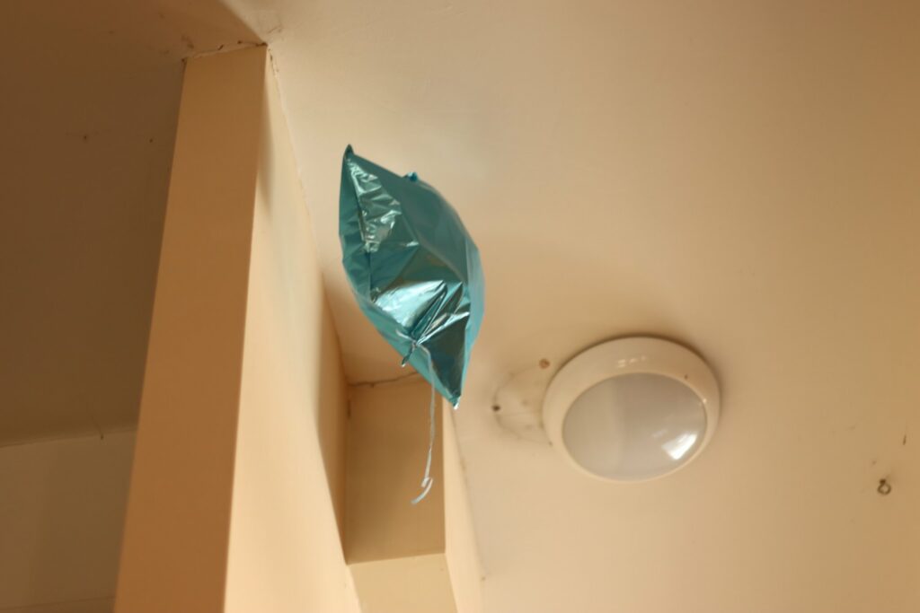 a turquoise foil balloon floats next to a ceiling light