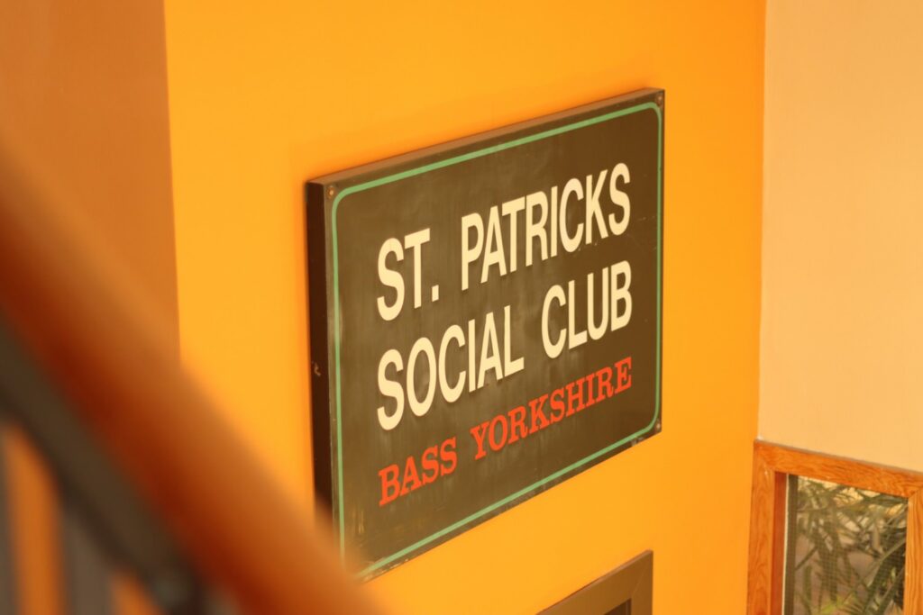 a sign reading 'Saint Patrick's Social Club, Bass Yorkshire' on a warm yellow wall