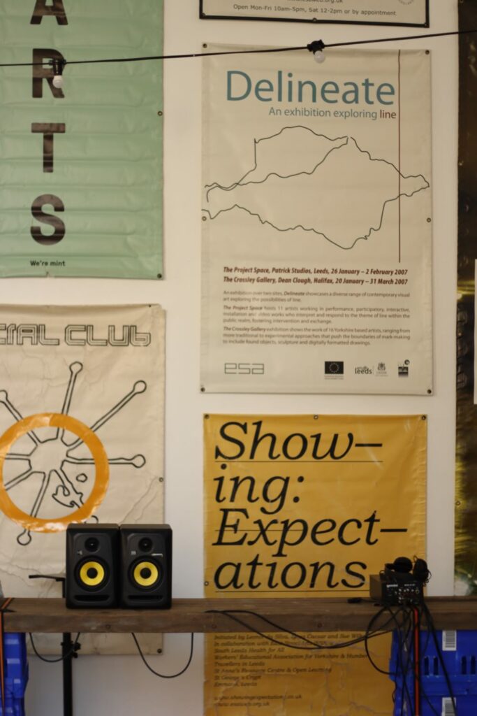 several posters for art exhibitions with two mini speakers on a shelf in front
