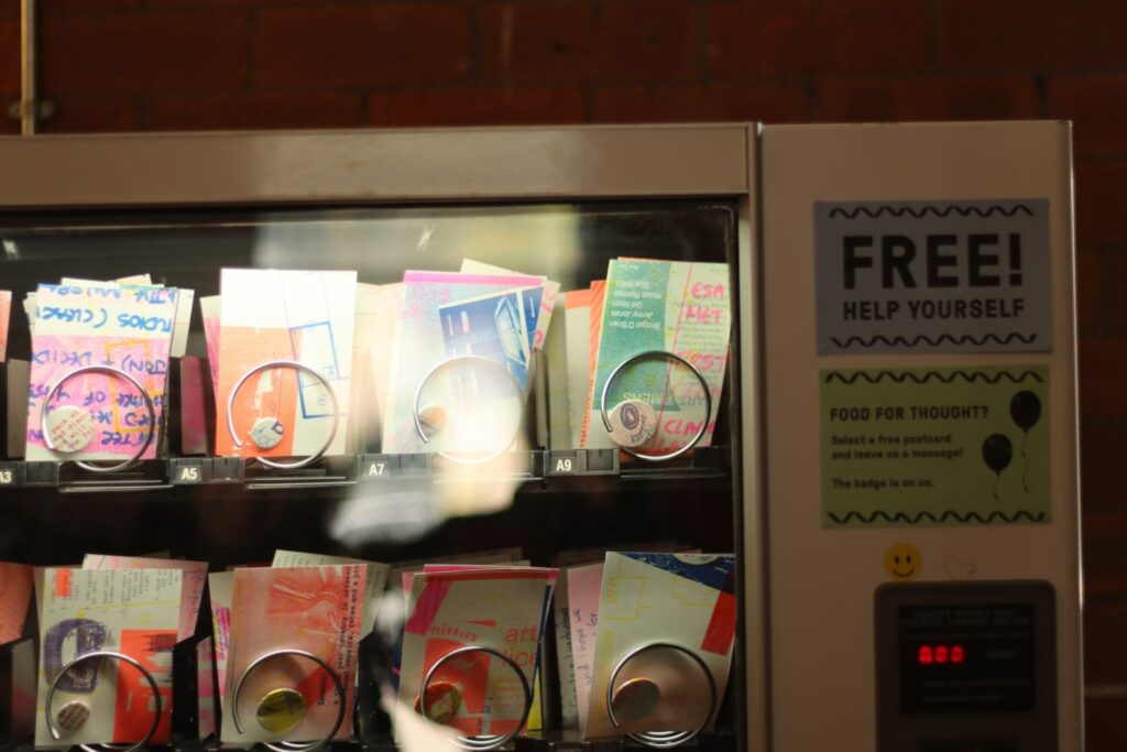 a vending machine with small prints where confectionary items for purchase would usually be. a sign on the side reads 'free, help yourself'.