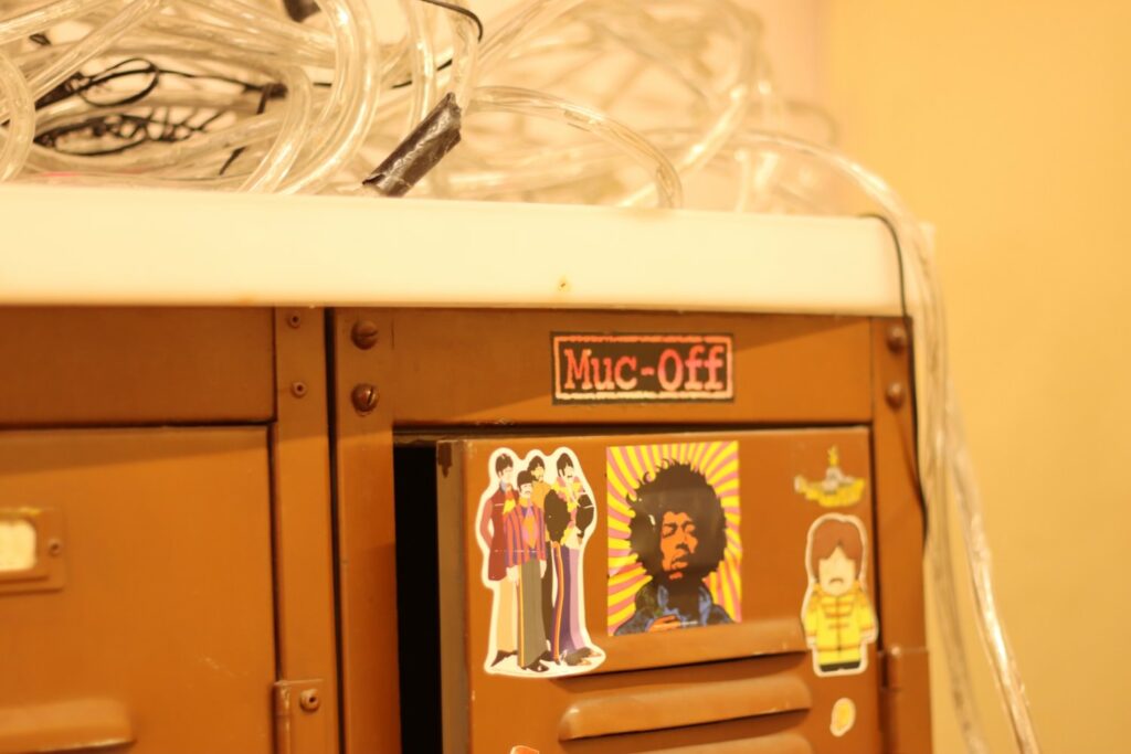 stickers depicting the beatles and Jimi Hendrix stuck to the top corner of brown metal lockers. 