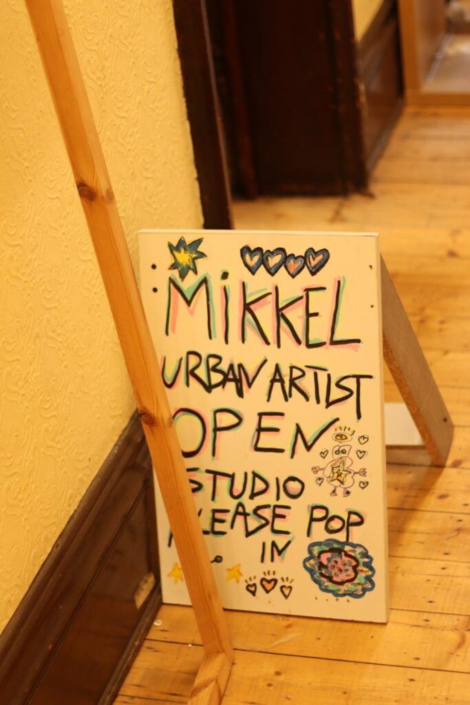 a handwritten sign reading 'mikkel urban artist open studio, please pop in' surrounded by colourful drawings of hearts and flowers