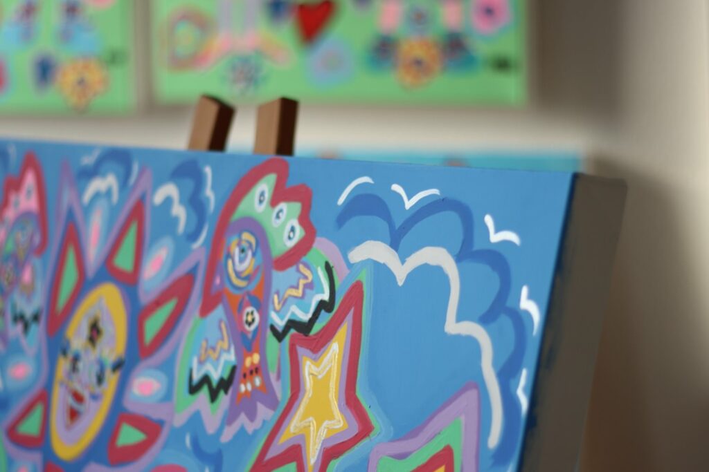 the top right corner of a canvas which has been placed on an easel. the artwork has a mid blue background and brightly coloured lines in the shape of clouds and a bird.