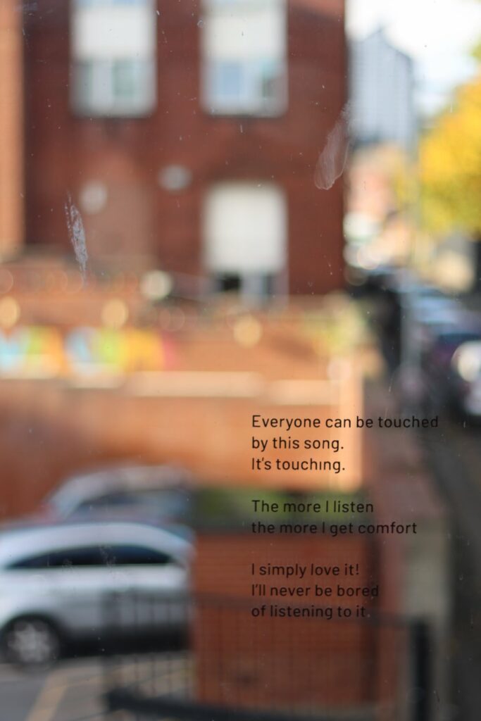 Text on a window reading " Everyone can be touched by this song. it's touching. the more I listen the more I get comfort. I simply love it! I'll never be bored of listening to it."