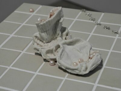 A sculpture of a solid white sock surrounded by pearls on beige ceramic tiles.